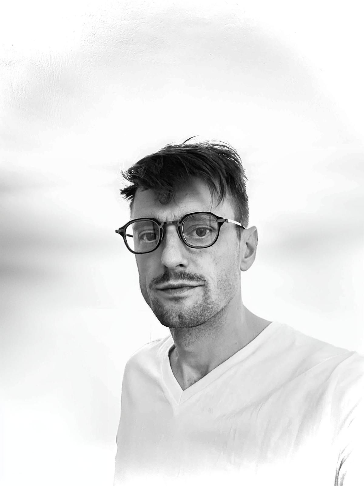 Tarik Abaspahic smiling and looking at the camera in a head-and-shoulders portrait; casual shirt in a home office with a blurred laptop and bookshelf in the background; friendly confident and approachable tone